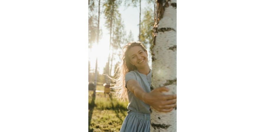 Foto: Initiative gute Luft. Frau umarmt Baum und freut sich über pollenfreie Luft.