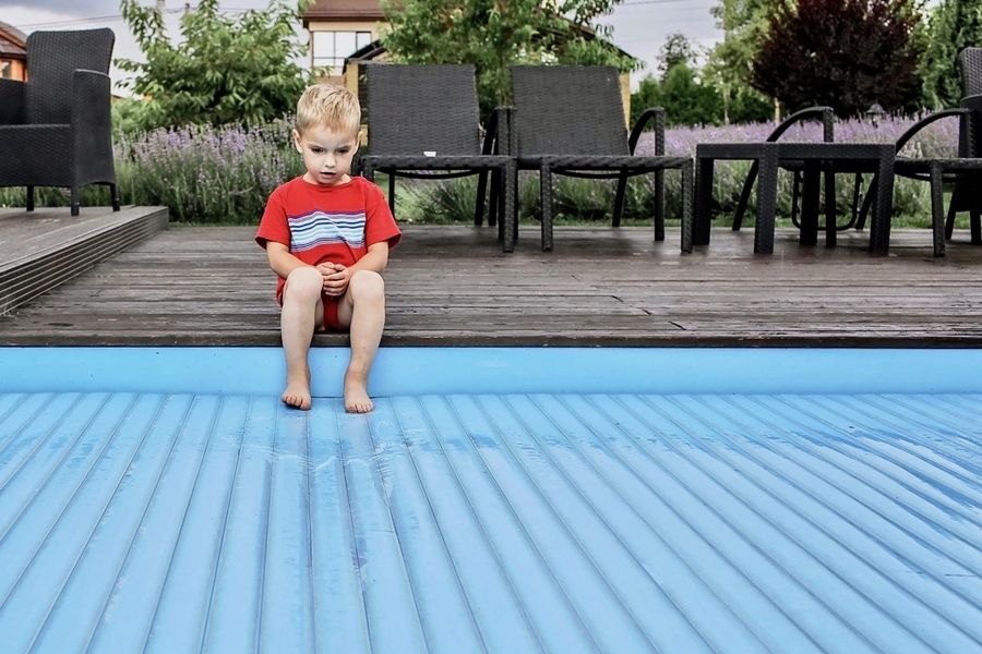 Kind sitzt am Rand eines abgedeckten Pools.